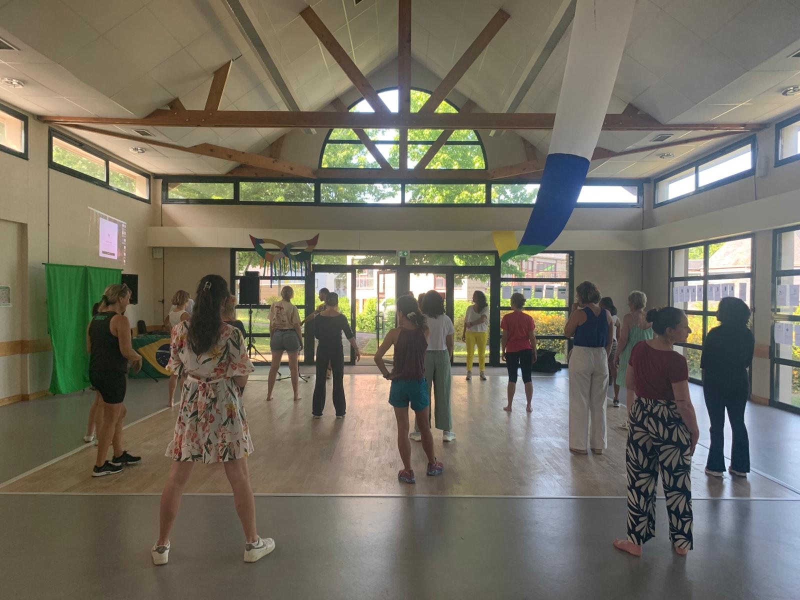 Une vingtaine de personnes debout dans une salle lumineuse, pendant l'atelier de danse du 14 juin